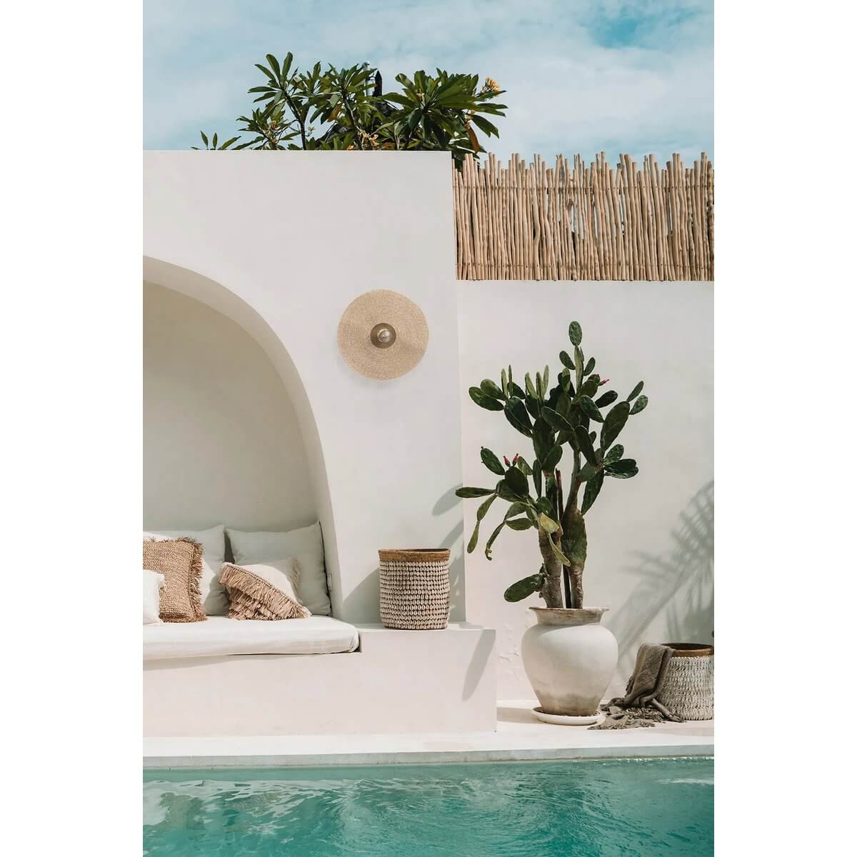 De Let's Groove Wandlamp - Natuurlijk Messing - M op witte muur naast zwembad en planten, voegt natuurlijke luxe toe aan buitenruimte.