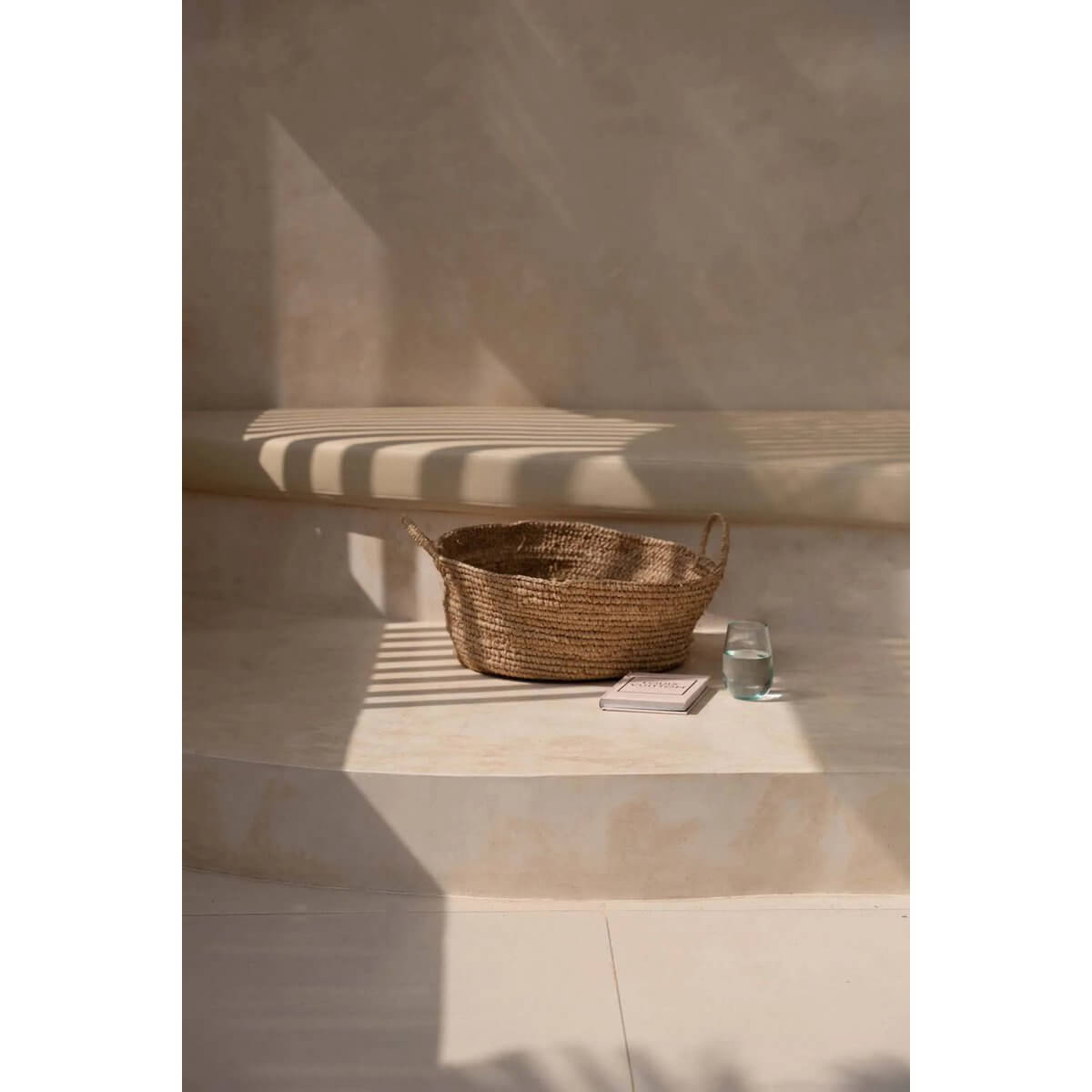 De Raffia Mandenbakken - Naturel - M in sunlight on a ledge, showcasing rustic elegance and natural beauty for small spaces.