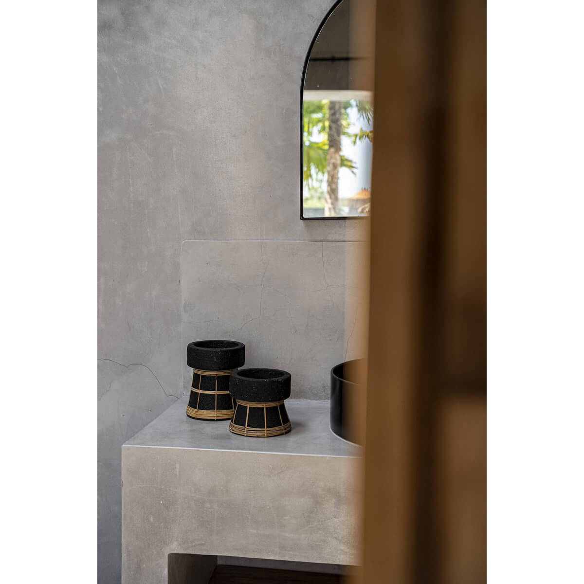 De Serene Kaarsenhouder - Zwart Naturel - S op een moderne tafel met rotan details, perfect voor sfeervolle decoratie in elk seizoen.